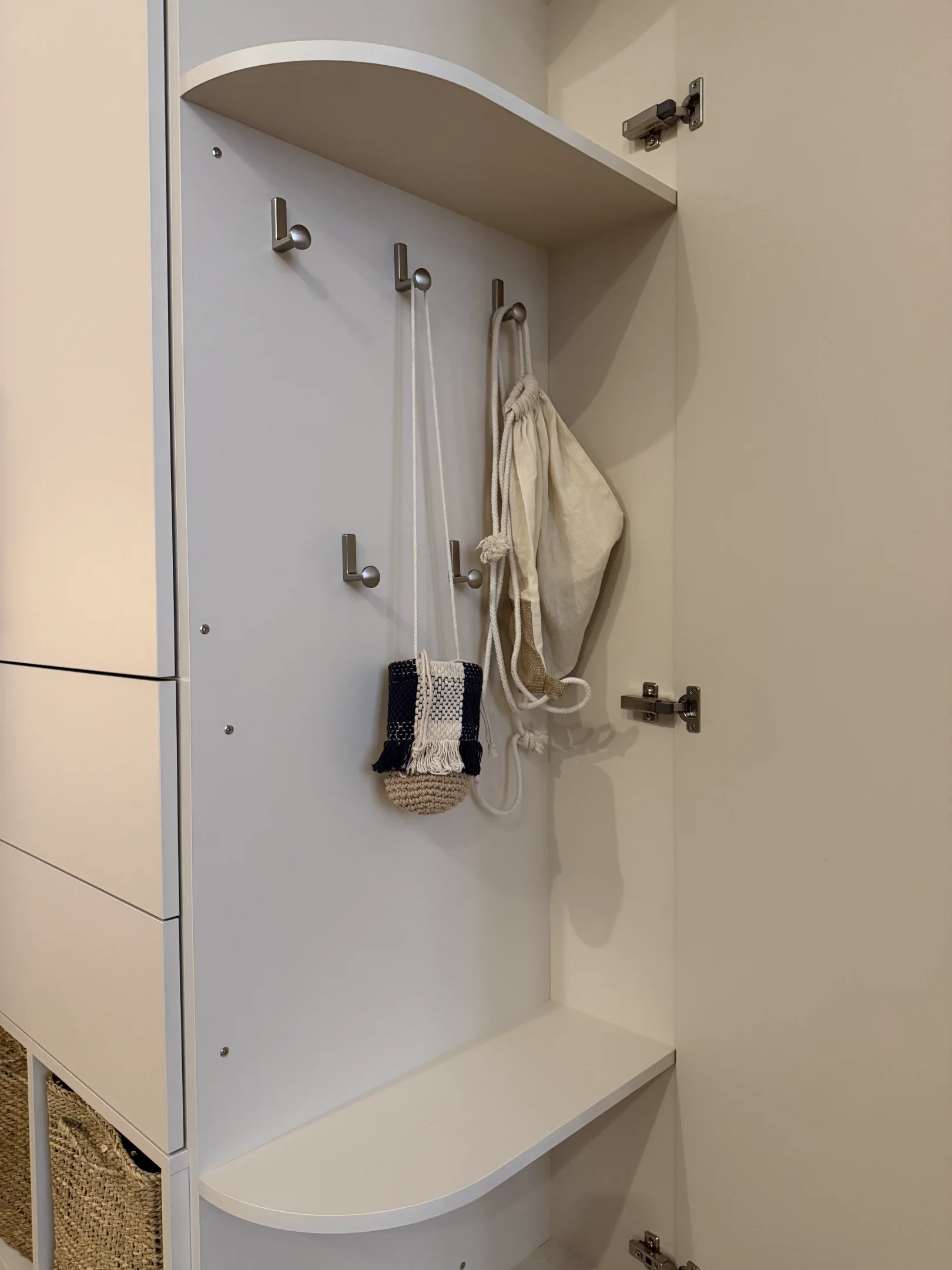 Bílý nábytek se skříňkou, háčky a taškami.